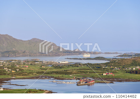 A cruise liner rests in a Norwegian fjord during golden hour, with rorbuer cabins along the shore A cruise liner rests in a Norwegian fjord during golden hour, with rorbuer cabins along the shore 110414402