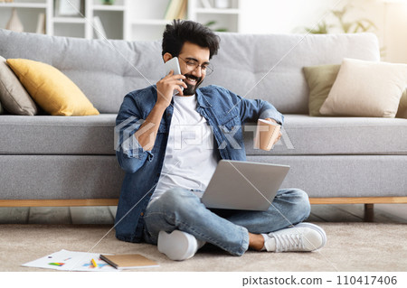 Indian man making phone call, drinking coffee and using laptop at home Indian man making phone call, drinking coffee and using laptop at home 110417406