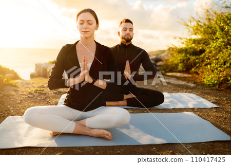 Man and woman meditating on yoga mats during sunset Man and woman meditating on yoga mats during sunset 110417425