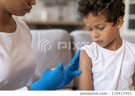 Doctor making vaccination against flu for little black boy in home interior 110417451