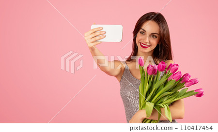 Vivacious woman with a captivating smile taking a selfie, holding a bouquet of pink tulips Vivacious woman with a captivating smile taking a selfie, holding a bouquet of pink tulips 110417454