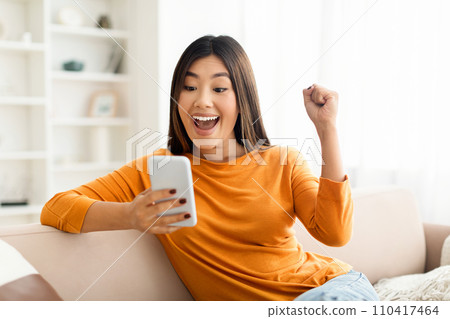 Overjoyed happy millennial asian woman celebrating success with smartphone Overjoyed happy millennial asian woman celebrating success with smartphone 110417464
