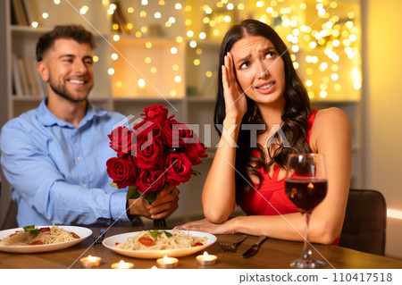 Man with roses smiling, woman stressed at dinner date Man with roses smiling, woman stressed at dinner date 110417518