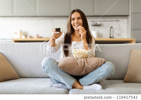Happy Young Woman Holding Remote Controller And Eating Popcorn At Home 110417542