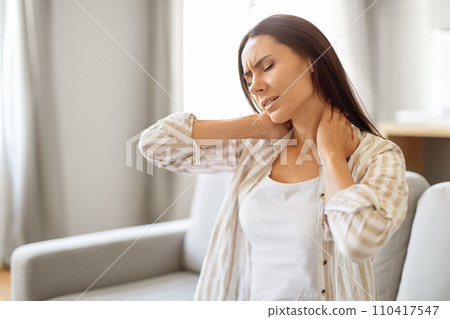 Young woman at home touching her neck with pained expression, 110417547