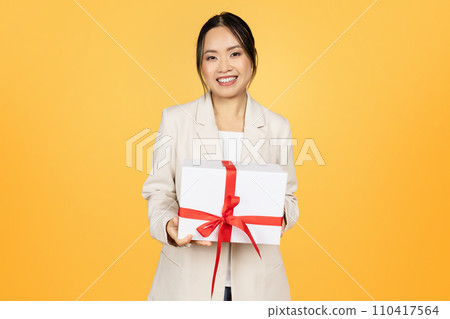 Smiling millennial japanese woman in suit shows box with gift 110417564