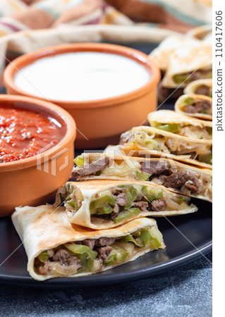 Fajita quesadilla with pieces of beef steak, green bell pepper, onion and cheese, on plate, closeup 110417606