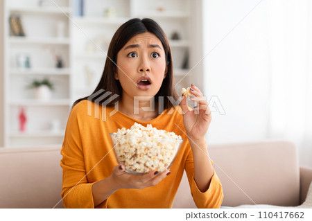 Closeup frightened young asian woman watching scary movie at home Closeup frightened young asian woman watching scary movie at home 110417662