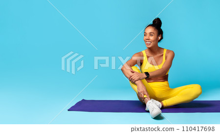athletic african american woman sitting on yoga mat, blue background 110417698