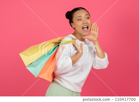 Asian woman holding shopping bags and making announcement with hand near mouth 110417700