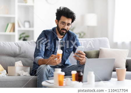 Young indian man holding bottle with pills and using smartphone Young indian man holding bottle with pills and using smartphone 110417704