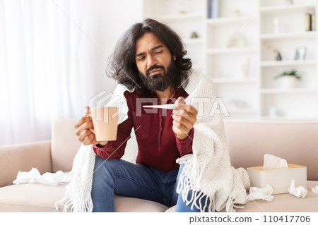 Unhealthy hindu guy checking body temperature, home interior Unhealthy hindu guy checking body temperature, home interior 110417706
