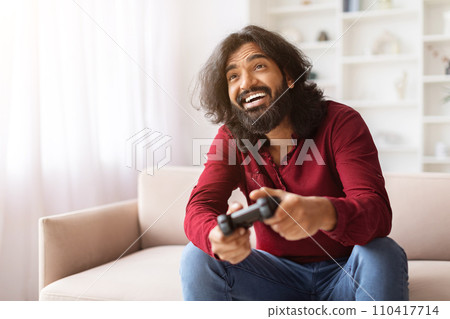 Emotional eastern guy playing video game with joystick at home 110417714