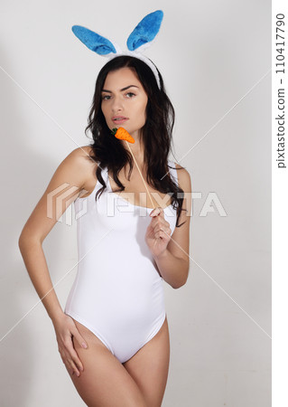 Beautiful woman with bunny ears and swimsuit with marzipan carrot. Easter desserts 110417790