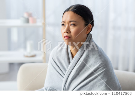 Depressed asian woman wrapped in blanket sitting on couch Depressed asian woman wrapped in blanket sitting on couch 110417803