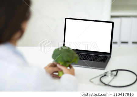 Doctor dietician have online consultation, using laptop, holding broccoli Doctor dietician have online consultation, using laptop, holding broccoli 110417916