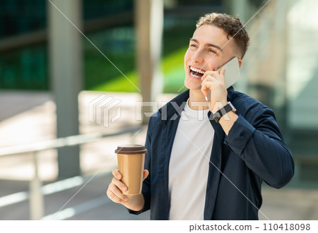 An exuberant young man in a navy blue jacket talking on a smartphone 110418098