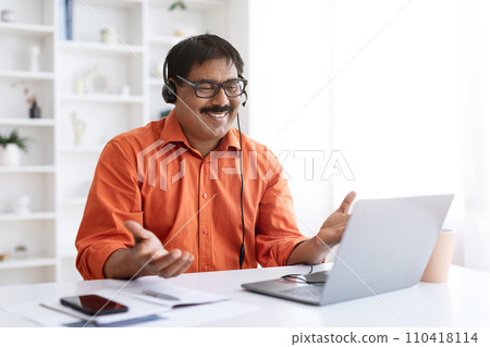 Smiling mature indian man using laptop and headset Smiling mature indian man using laptop and headset 110418114
