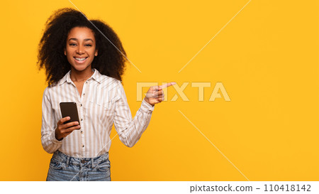 Happy black lady with phone pointing sideways at free space on yellow Happy black lady with phone pointing sideways at free space on yellow 110418142