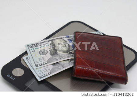 Brown wallet with banknotes on electronic kitchen scales. Symbol of accounting and family finance planning. Brown wallet with banknotes on electronic kitchen scales. Symbol of accounting and family finance planning. 110418201