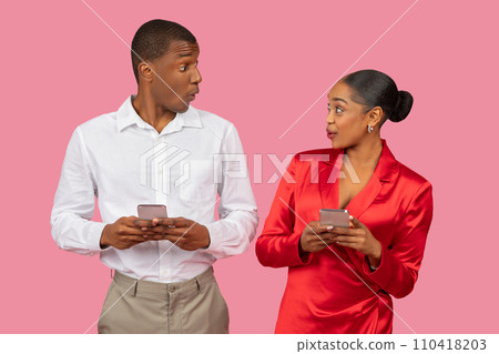 Surprised black couple with smartphones, both in holidays attire looking at each other Surprised black couple with smartphones, both in holidays attire looking at each other 110418203