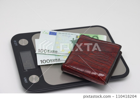 Brown wallet with banknotes on electronic kitchen scales. Symbol of accounting and family finance planning. Brown wallet with banknotes on electronic kitchen scales. Symbol of accounting and family finance planning. 110418204