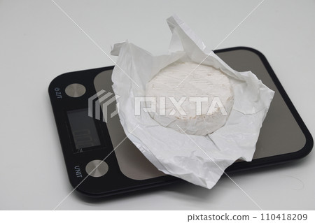 A piece of cheese on the scales. Weight loss, diet and weight control. Still life with healthy food and scales. Healthy food. The concept of a healthy lifestyle. Weight control during self isolation. 110418209