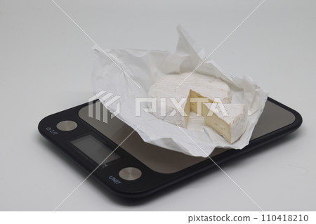 A piece of cheese on the scales. Weight loss, diet and weight control. Still life with healthy food and scales. Healthy food. The concept of a healthy lifestyle. Weight control during self isolation. A piece of cheese on the scales. Weight loss, diet and weight control. Still life with healthy food and scales. Healthy food. The concept of a healthy lifestyle. Weight control during self isolation. 110418210