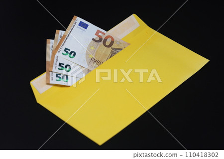 Banknotes in a yellow envelope on a black background. Bribery concept. Salary in envelopes. Financial fraud. Close up 110418302