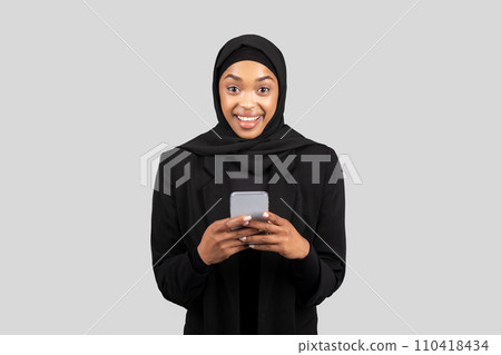 Smiling surprised millennial black lady in hijab chatting on smartphone in social networks 110418434