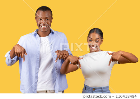 Joyful black couple pointing down, prideful smiles, yellow background Joyful black couple pointing down, prideful smiles, yellow background 110418484