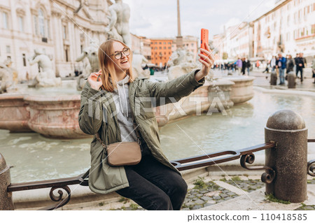 A happy blond woman tourist is standing of the famous Piazza Navona in Rome, Italy. Concept of traveling famous landmarks. 30s Women taking selfie 110418585