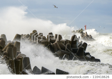 Storm at sea, high waves crashing against the concrete breakwaters of the port, high white splashes 110418626