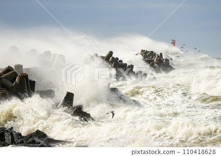 Storm at sea, high waves crashing against the concrete breakwaters of the port, white splashes Storm at sea, high waves crashing against the concrete breakwaters of the port, white splashes 110418628