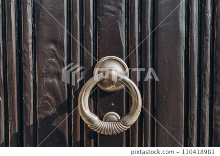 Antique brass door knocker in the shape, door element with metal knob. A old door handle on a vintage wooden black door Antique brass door knocker in the shape, door element with metal knob. A old door handle on a vintage wooden black door 110418981