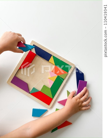 childs hand collects multicolored wooden mosaic on white background. childs hand collects multicolored wooden mosaic on white background. 110419341