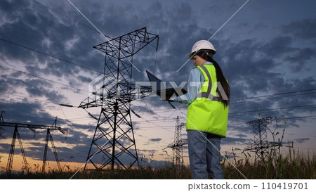 Woman technician types on laptop keyboard walking to power transmission lines Woman technician types on laptop keyboard walking to power transmission lines 110419701