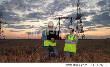Electricians with laptop discuss innovative solution by power transmission lines Electricians with laptop discuss innovative solution by power transmission lines 110419702
