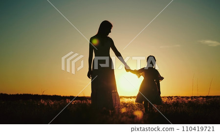 Mamma and daughter enjoying sunset in nature while walking in sun-drenched field 110419721