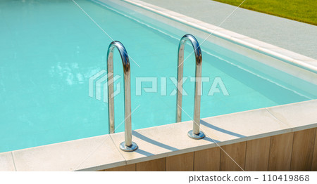 Grab bars ladder in the blue swimming pool. Ladder stainless handrails for descent into swimming pool. Vacation concept Grab bars ladder in the blue swimming pool. Ladder stainless handrails for descent into swimming pool. Vacation concept 110419868