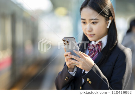戴著耳機的高中女生看著智慧型手機螢幕，專注於手 110419992