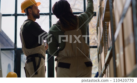 Hip level shot of warehouse manager and trainee performing inventory check, keeping quality standards high. Proactive experts in depot prepare to ship parcels, crosschecking delivery info 110420770