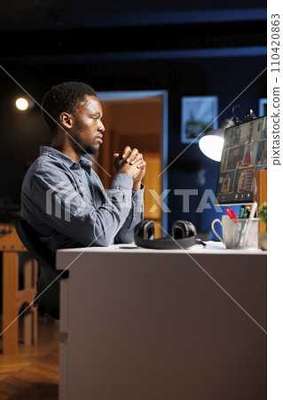 Student attending online course lesson on videocall at home, meeting with colleagues and teacher to discuss about new class work. African american man listens to tutor talk about business program. 110420863