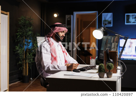 Arab entrepreneur participates in online video sessions at the office table. While using a digital desktop pc for communication and research a Muslim man pays great attention to his coworkers. 110420897