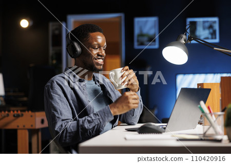 Developer working on new project and enjoying live podcast at home, feeling pleased with personal program and new freelance contract. African american guy attends online e learning program. 110420916