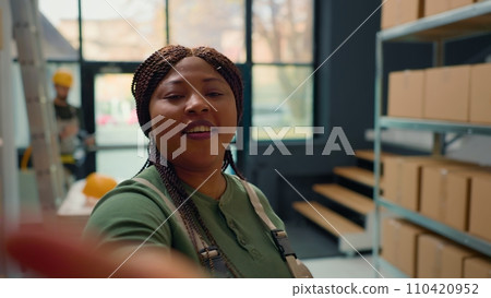 African american warehouse head of logistics using selfie smartphone camera, filming introduction video for new interns starting job in storage facility, teaching them safety measures 110420952