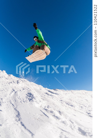 Snowboarder jumping against blue sky Snowboarder jumping against blue sky 110421522