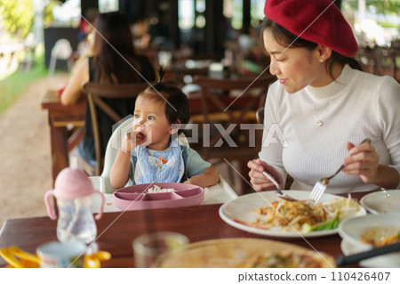 mother with toddler girl eating food and vegetable by self feeding BLW or baby led weaning on highchair in restaurant 110426407