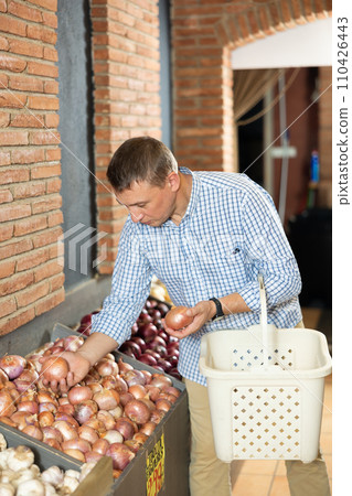 Man chooses onions for purchase in greengrocer shop 110426443