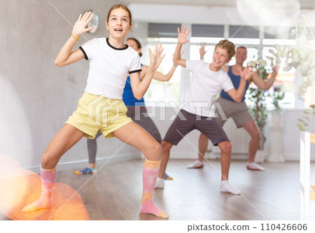 Cheerful friendly school children spreading hands wild apart while practicing active dance with their middle-aged parents in dance hall Cheerful friendly school children spreading hands wild apart while practicing active dance with their middle-aged parents in dance hall 110426606
